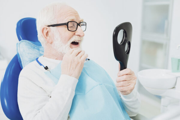 Ready to eat. Attentive senior man touching his mouth while carrying mirror