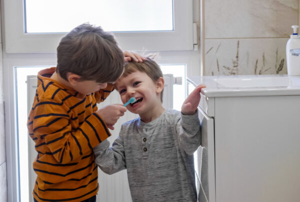 Cute boy helps his smaller brother brushing teeth