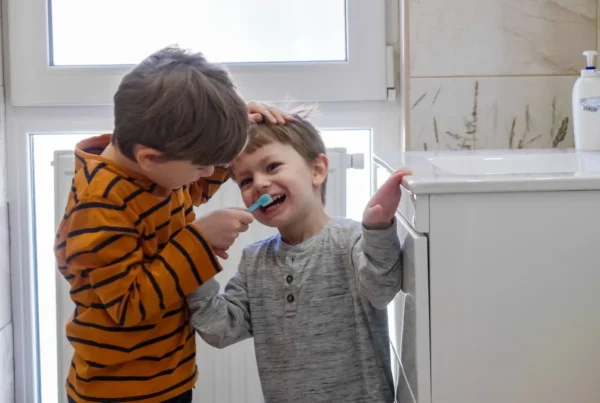 Cute boy helps his smaller brother brushing teeth